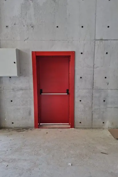 Beton duvarda panik barlı kırmızı çelik yangın kapısı
